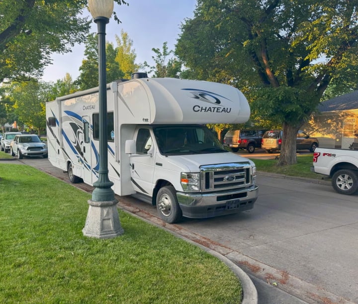 A white Thor Chateau Class C rv rental is parked on a residential street next to a green lawn.. Thor Chateau 2023