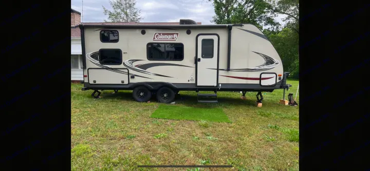 A beige Coleman travel trailer, ready for your next adventure as an RV rental, parked on grass with leveling jacks extended.. Coleman 2125bh 2019