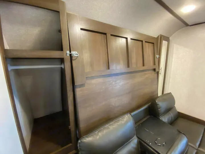 RV rental interior: Wooden closet with hanging rod, and black leather reclining seating with a console.. Coleman 2125bh 2019