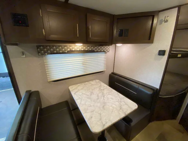 This RV rental interior features a functional dinette with a marble-look table & black benches, plus overhead storage.. Coleman 2125bh 2019