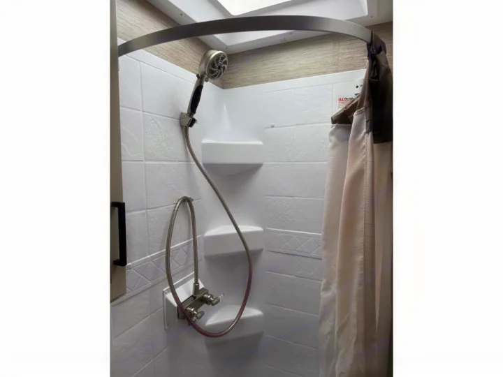 Clean RV rental shower featuring a handheld showerhead, temperature controls, and privacy curtain.. Thor Axis 2022