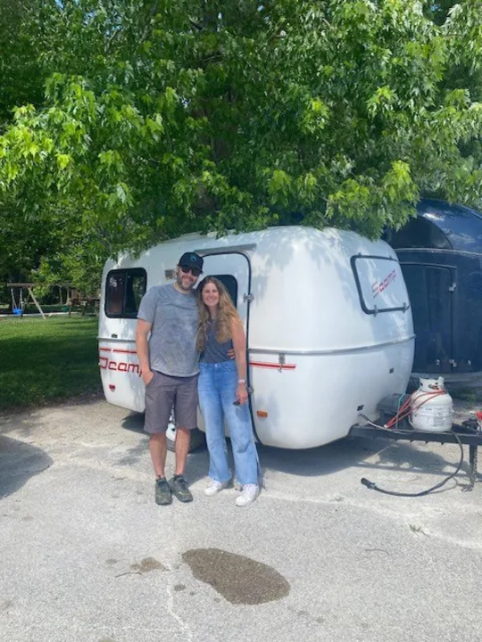 A happy couple stands beside their white Scamp travel trailer, an ideal compact rv rental for outdoor adventures.. Scamp Scamp Trailer 1999