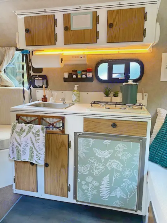Modern RV rental kitchen setup with sink, stove, & a unique botanical-themed fridge. Organized & inviting space.. Scamp Scamp Trailer 1999