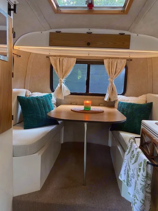 This inviting RV rental interior features a cozy dinette with a wood table, benches, and soft lighting, perfect for travel.. Scamp Scamp Trailer 1999