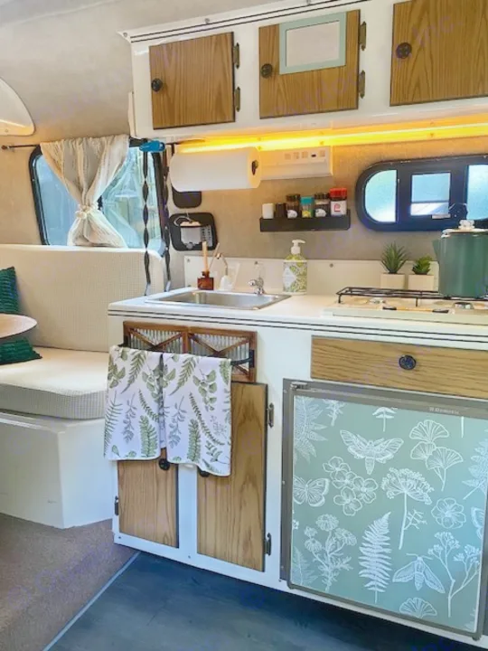 This cozy RV rental interior features a compact kitchen with sink, stovetop, and fridge, plus a comfy bench seat.. Scamp Scamp Trailer 1999