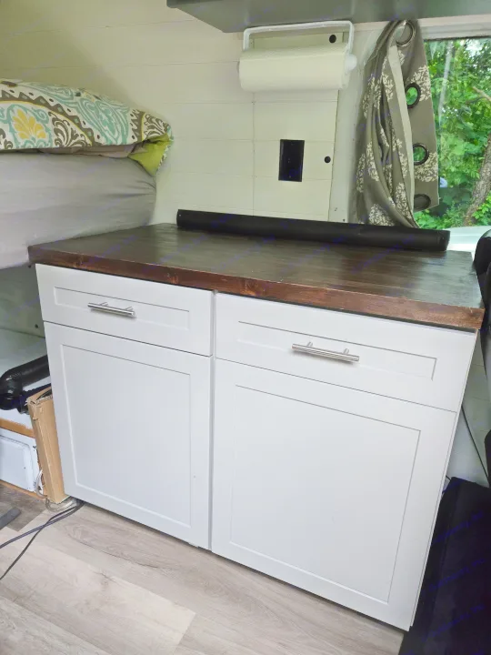 RV rental interior: light gray cabinets, dark wood counter, and patterned bed. Efficient storage in a cozy travel space.. Freightliner Sprinter 2011