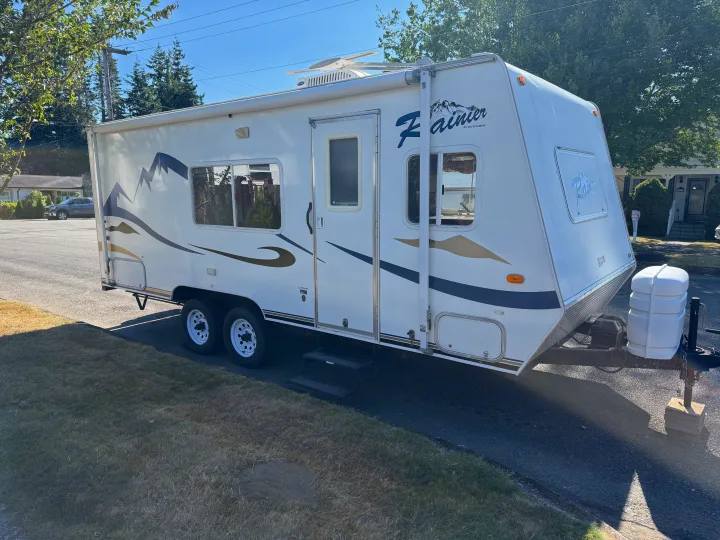 A white travel trailer RV with mountain graphics, available as an RV rental, parked on a sunny street.. Dutchmen Rainier 2006