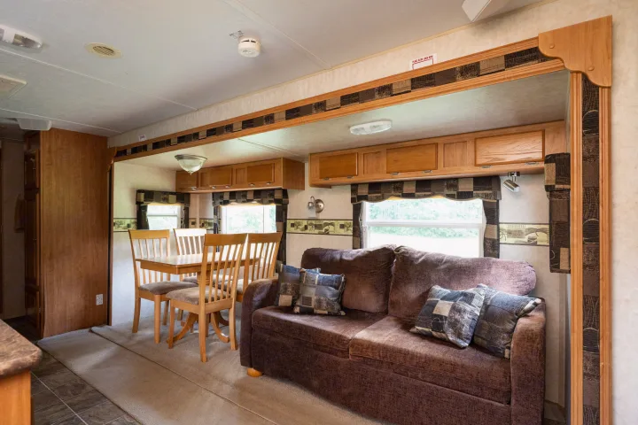 Clean RV rental interior with brown sofa, light wood dining table & chairs, and overhead cabinets. Ideal for travel.. Forest River Rockwood Signature Ultra Lite 2009