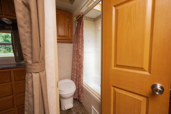 Inside an RV rental, a functional bathroom features a white toilet, patterned shower curtain, and wood cabinets, designed for compact living.. Forest River Rockwood Signature Ultra Lite 2009