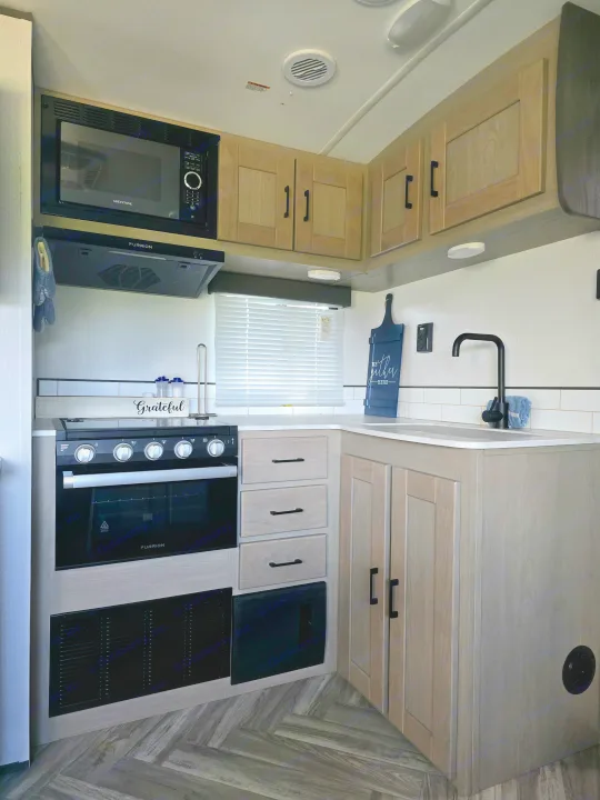 Bright RV rental kitchen: Greystone microwave, Furrion oven, black sink faucet, and light wood-look cabinets.. Cruiser RV Shadow Cruiser 2021