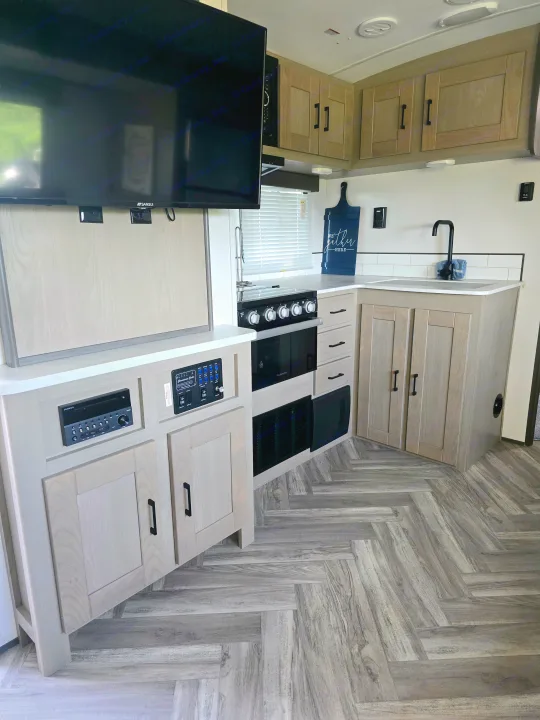 Modern RV rental kitchen featuring light wood cabinets, TV, stove, sink, and an integrated control panel, ideal for comfortable travel.. Cruiser RV Shadow Cruiser 2021