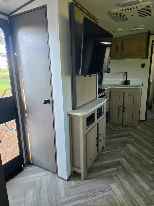 Modern RV rental interior showing a compact kitchen with gray cabinets & sink, entertainment center with TV, and stylish herringbone flooring.. Cruiser RV Shadow Cruiser 2021