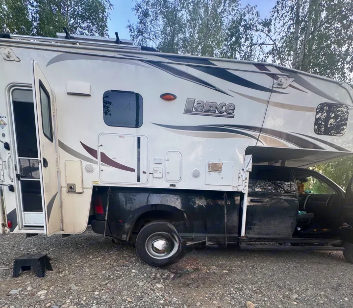 This white Lance truck camper, a type of RV rental, is ready for adventure. Open door & outdoor step visible.. Lance 1172 2017