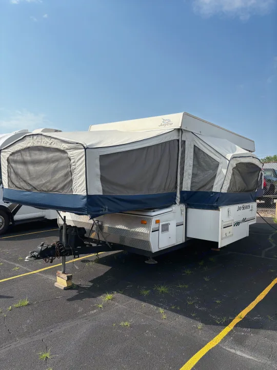 This Jayco pop-up camper, an ideal RV rental, is parked with tent sections extended under a clear sky on an asphalt lot.. Jayco Jay Series 2006