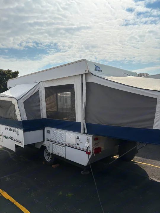 This white and blue Jayco pop-up camper, set up and ready for an RV rental adventure, sits under a cloudy sky.. Jayco Jay Series 2006