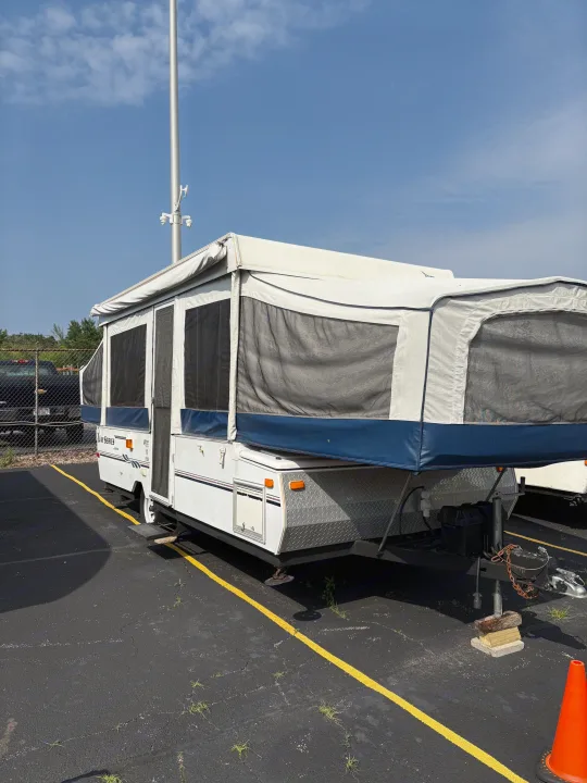 Pop-up camper RV rental: A white & blue pop-up trailer with screen windows parked outdoors under a blue sky.. Jayco Jay Series 2006