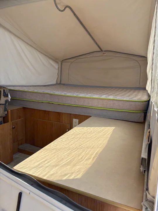 Interior of a pop-up camper rv rental, featuring a raised bed with mattress, wooden cabinets, and a lower platform.. Jayco Jay Series 2006