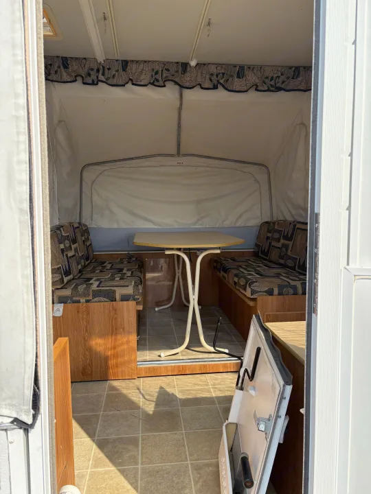 RV rental interior: Pop-up camper dinette with patterned seats, a table, tiled floor, and wood-look trim.. Jayco Jay Series 2006