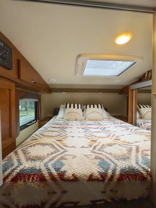 Cozy RV rental bedroom interior with patterned blanket, skylight, and window view.. Lance 1172 2017