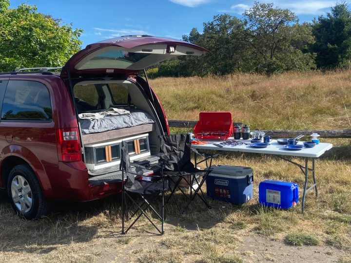 Minivan converted for camping, with a cozy bed, outdoor camp kitchen, chairs, and cooler. Perfect RV rental for road trips!. Dodge Grand Caravan 2010