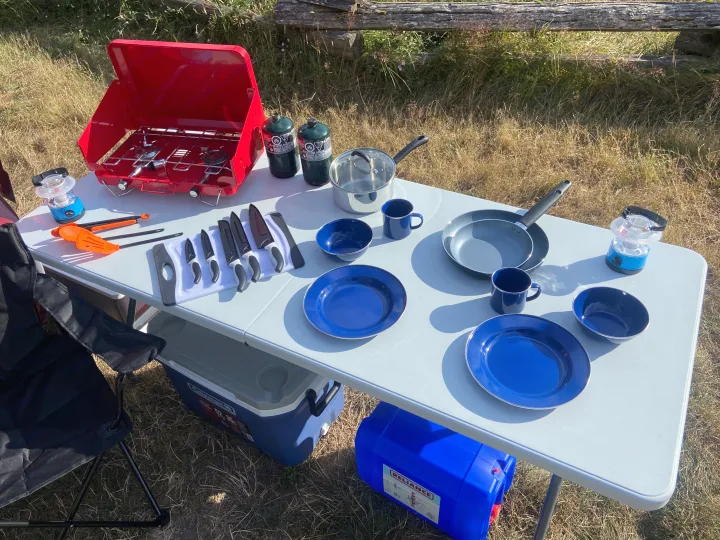 RV rental outdoor cooking: Portable stove, cookware, blue dishes, and camp gear organized on a table for meals.. Dodge Grand Caravan 2010