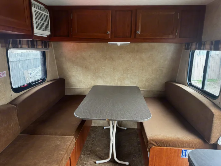 RV rental interior: A comfortable dinette with brown benches, a grey table, and wooden overhead cabinets.. Jayco Jay Flight Swift SLX 2012