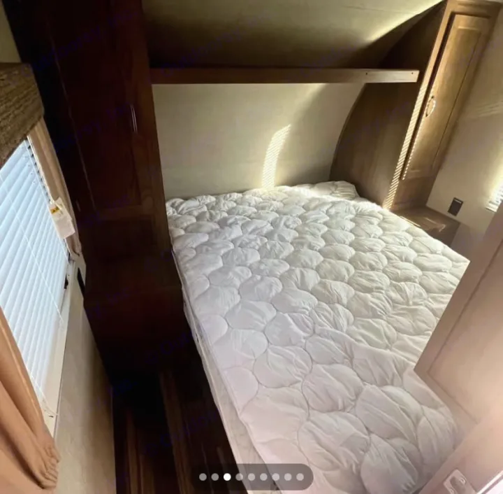 Inside an RV rental: a clean, cozy bedroom with a white quilted bed, overhead storage, and sunlit window.. Gulf Stream Conquest 2017