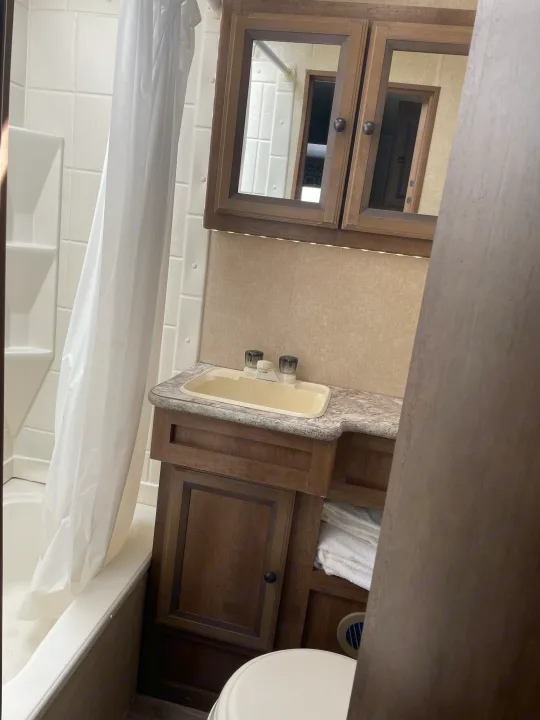 Compact RV rental bathroom: features white tub/shower, vanity with sink, cabinets, and toilet area.. Cruiser RV Radiance 2015