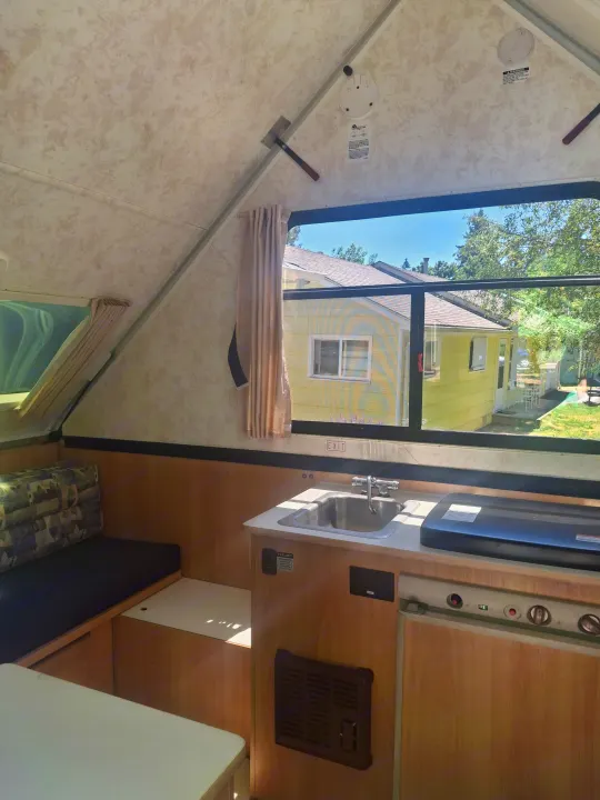 Inside a cozy RV rental camper, featuring a compact kitchen with sink, dining bench, and a window view.. Chalet Chalet Popup Trailer 2006