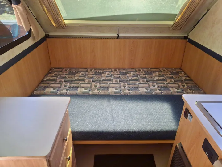 RV rental interior features a cozy bed/dinette, light wood counters, and a pop-up roof with ample natural light.. Chalet Chalet Popup Trailer 2006