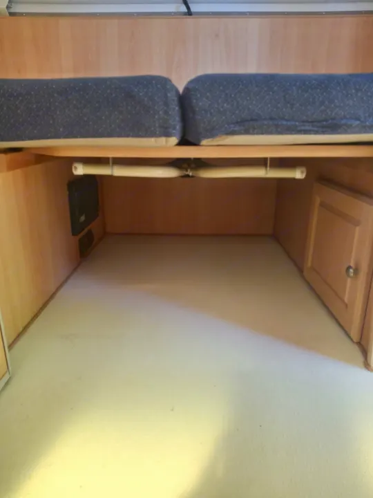 RV rental interior: cozy sleeping area with storage, featuring light wood, dark cushions & a small cabinet.. Chalet Chalet Popup Trailer 2006