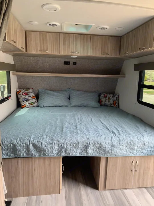 RV rental bedroom showcasing a cozy bed with blue bedding, overhead cabinets, and under-bed storage.. Minnie Micro Minnie 2021