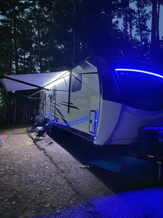 Night view of a brightly lit RV rental at a campground, featuring blue and white LED lights. Perfect for a fun camping trip!. Venture Rv SPORTTREK TOURING EDITION 2025