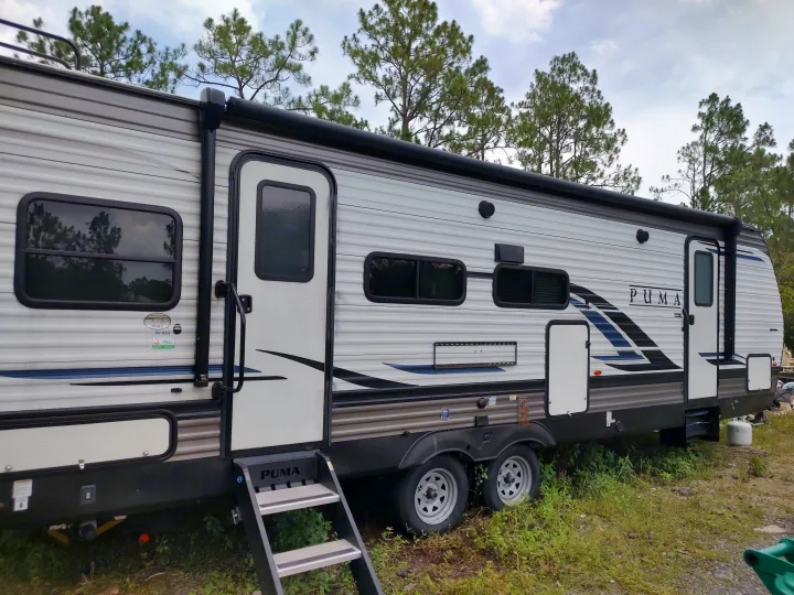 Side view of a PUMA travel trailer, an ideal rv rental option. Features an awning, multiple windows, and entry steps.. Palomino Puma 26RLS 2022