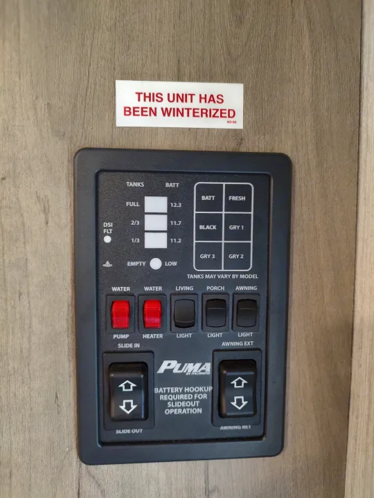 An RV rental's control panel: displays for tanks/battery, and switches for water, lights, slide-out, and awning. "THIS UNIT HAS BEEN WINTERIZED" notice.. Palomino Puma 26RLS 2022