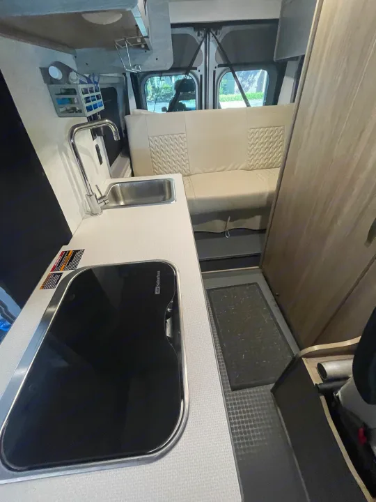 RV rental interior: Kitchen with sink, Suburban cooktop, overhead storage, and textured bench seating.. Winnebago Winnebago Solis P 2022