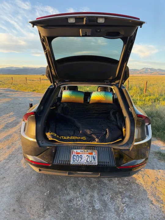 Car camping in an electric vehicle, bedding ready for adventure. A cat watches from beside this smart alternative to an rv rental.. Kia EV6 Wind All Wheel Drive 2022