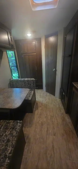 RV rental interior: A compact dinette with patterned cushions, wood-look floor, and a window view of nature.. KZ Sportsman Classic 180 QB 2018