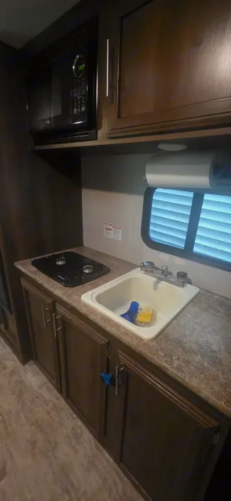 RV rental kitchen: microwave, two-burner stove, sink, dark wood cabinets. Compact galley space for your travels.. KZ Sportsman Classic 180 QB 2018