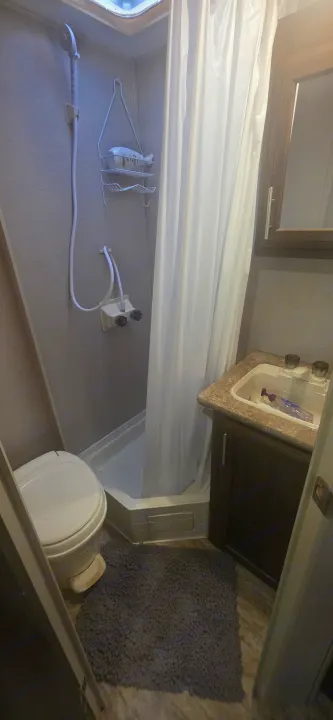Compact RV rental bathroom featuring a toilet, shower stall with white curtain, and sink vanity with mirror.. KZ Sportsman Classic 180 QB 2018