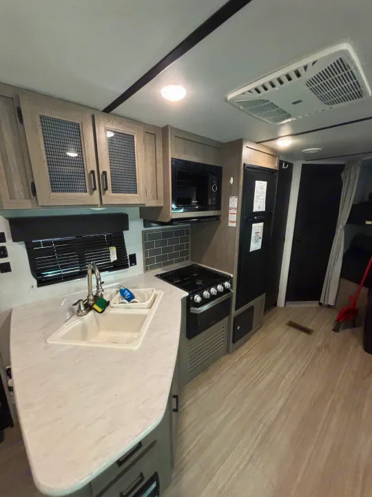 RV rental interior features a kitchen with a white sink, counter, and light wood cabinets, plus appliances like a microwave and stove.. Keystone Hideout 2020