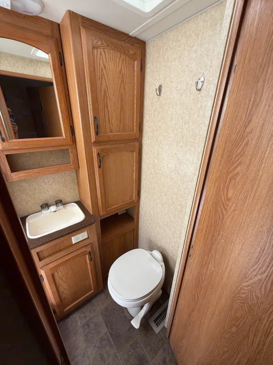 RV rental bathroom with sink, mirror, toilet, wooden cabinets, and wall hooks.. Denali Denali Trailer 2011