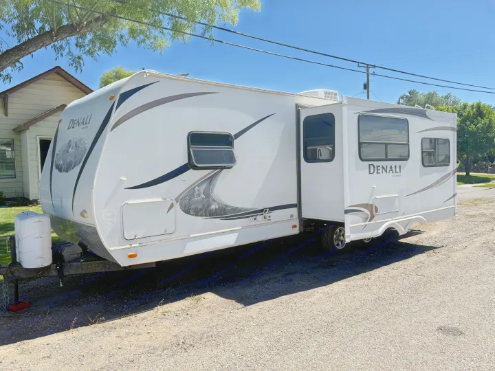 White Denali travel trailer (RV rental) parked on gravel, with slide-out extended, under a clear sky.. Denali Denali Trailer 2011