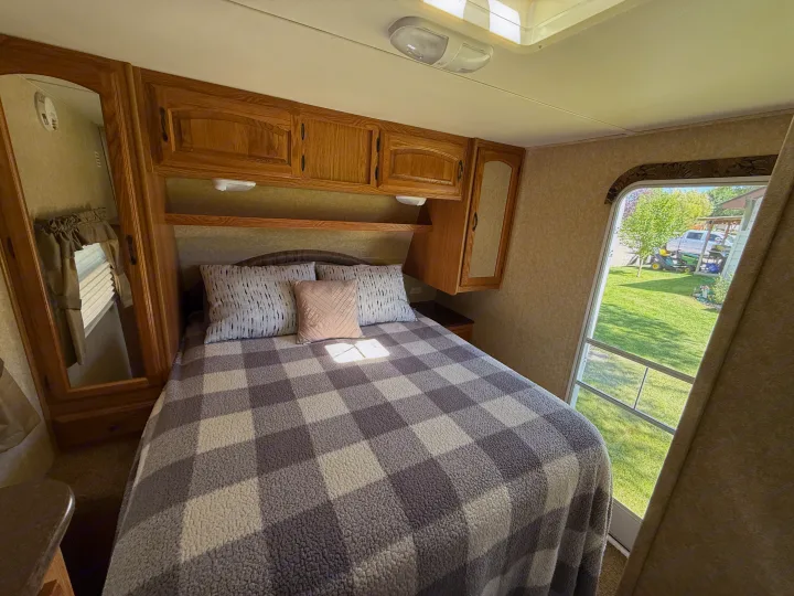 Cozy RV rental bedroom featuring a comfy bed, wooden cabinetry, and a bright window view of the scenic outdoors.. Denali Denali Trailer 2011