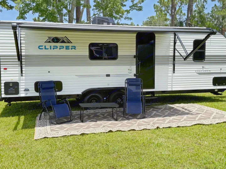 White & gray Clipper travel trailer (RV rental) with an awning, two lounge chairs, small table, and outdoor mat setup.. Coachmen Clipper 25BH 2025