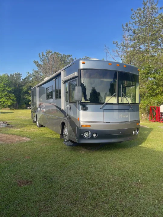 A modern gray and silver Horizon RV rental is parked on a lush green lawn under a bright blue sky, ready for adventure.. Itasca Horizon 2002