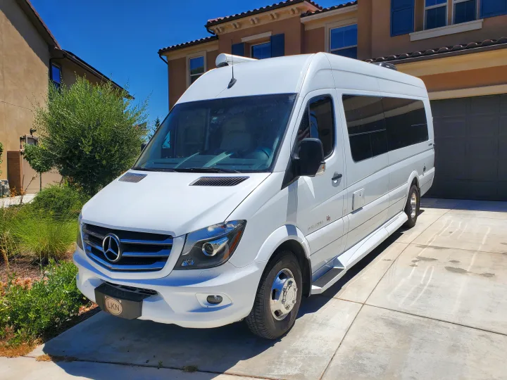 A white Mercedes-Benz Sprinter camper van, an RV rental, awaits adventure in a sunny driveway. Ideal for road trips!. Coachmen Galleria 2019