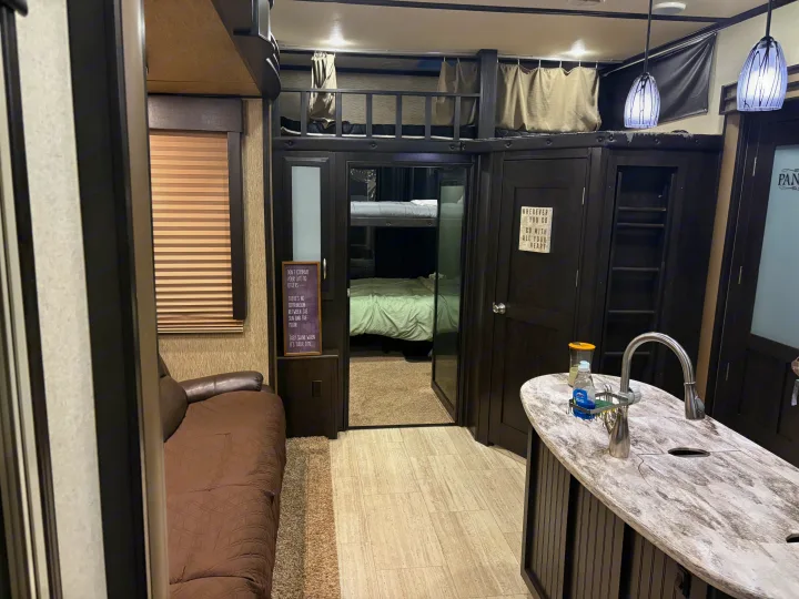Spacious RV rental interior featuring cozy bunk beds, a sofa, and kitchen island, ready for your next adventure.. Grand Design Momentum Toy Hauler 2015
