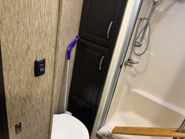 RV rental bathroom: compact design with a beige shower, dark cabinets, toilet, and a purple cleaning tool nearby.. Grand Design Momentum Toy Hauler 2015