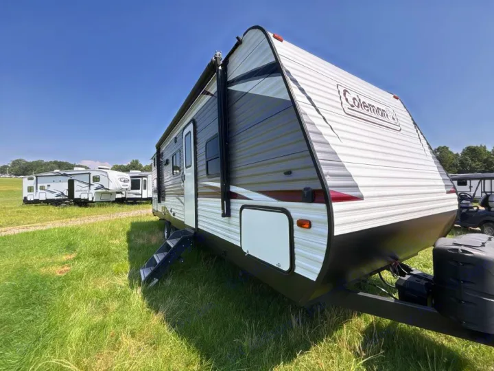 A Coleman travel trailer, ideal for an rv rental, parked on green grass under a blue sky, with other RVs in the background.. Dutchmen Coleman Lantern LT 2020